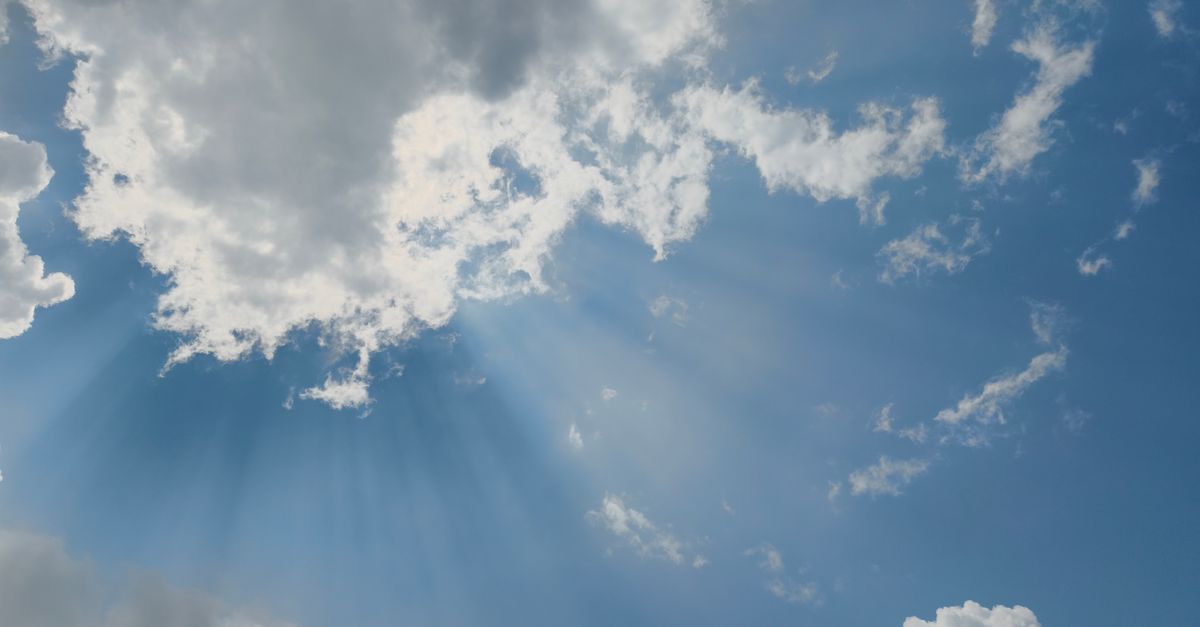 Beautiful sun rays streaming through fluffy clouds in a clear blue sky, captured in Silchar, India.